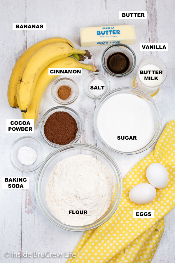 A white board with bowls of ingredients needed to make a chocolate banana cake.