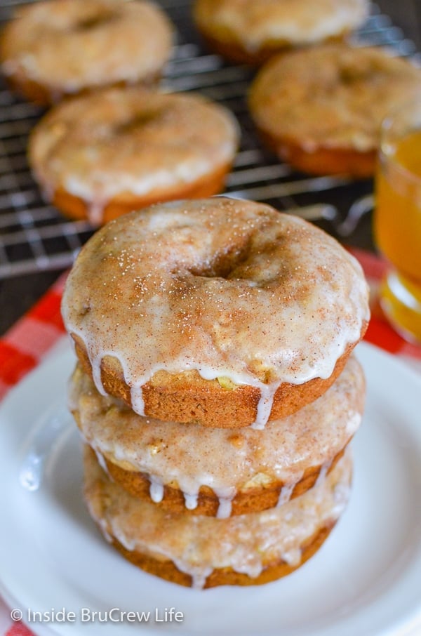 Three cinnamon apple donuts on a white plate with more donuts behind them