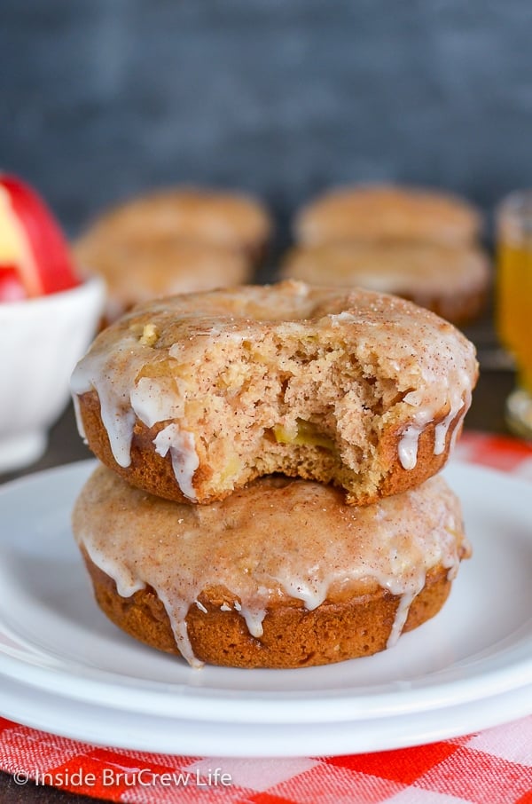 A white plate with two cinnamon apple donuts on it and a bite take out of the top donut