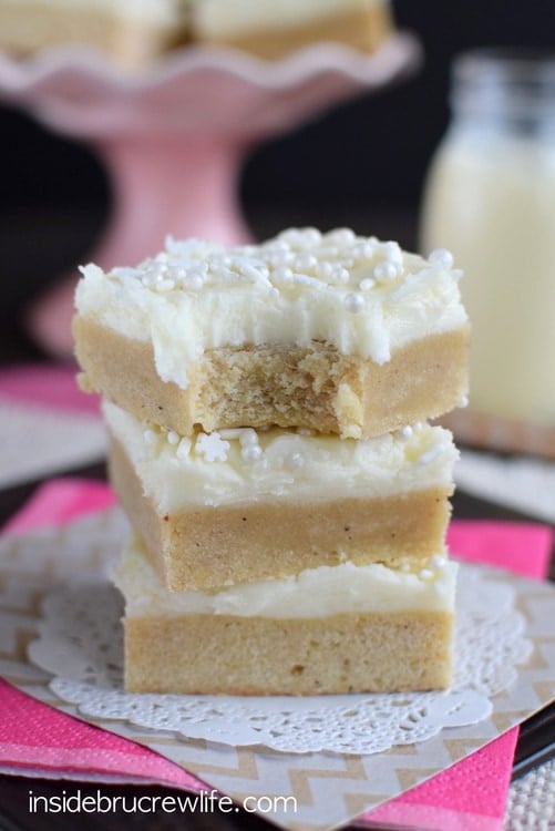 Three eggnog cookie bars topped with frosting and sprinkles stacked on top of each other.