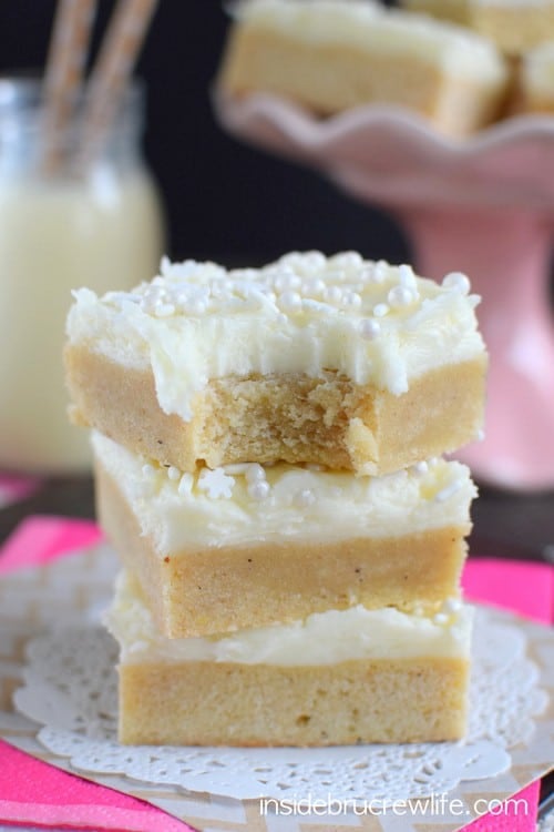 A stack of three eggnog bars topped with frosting on a white paper.