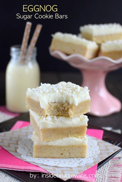 A stack of three eggnog bars topped with frosting and sprinkles on a white and pink paper.