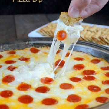 Cheesy pizza dip with a cracker being dipped into it.