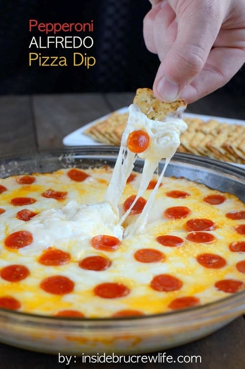 A pan of pizza dip with a cracker being dipped into it.