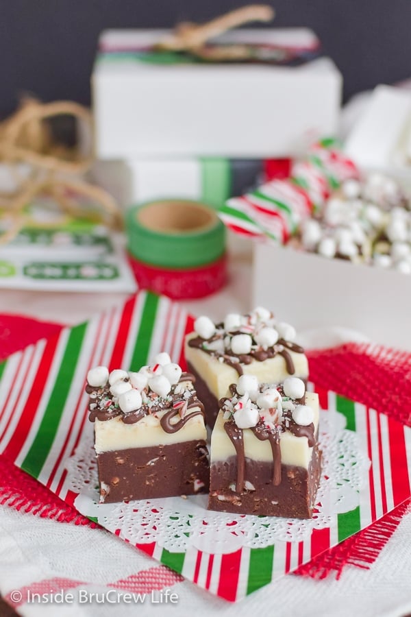 Three squares of hot chocolate fudge topped with candy canes and mini marshmallows on red and green paper.