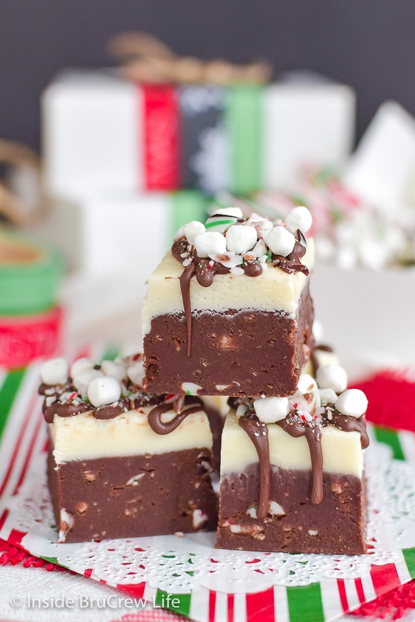 Three squares of hot chocolate fudge topped with chocolate, candy canes, and mini marshmallows on red and green paper.