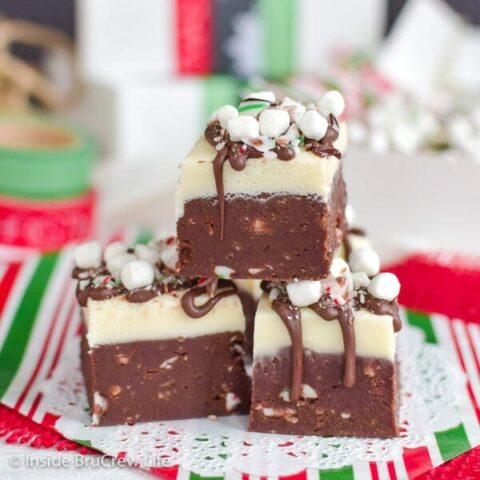 Three pieces of hot chocolate fudge topped with candy canes and mini marshmallows stacked up.