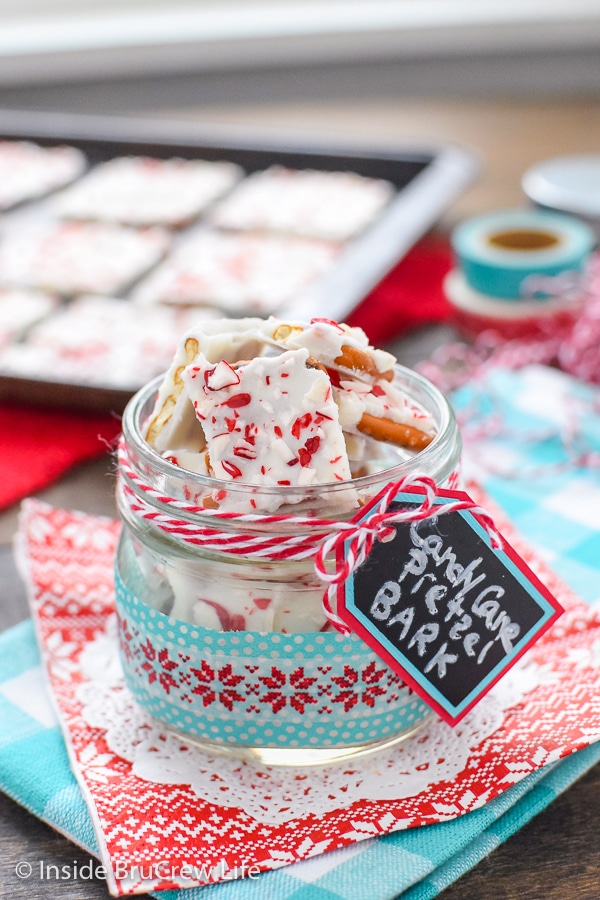 A clear jar filled with pieces of candy cane pretzel bark and tray of more bark behind it