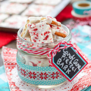 A clear jar filled with candy cane pretzel bark on a red and teal towel