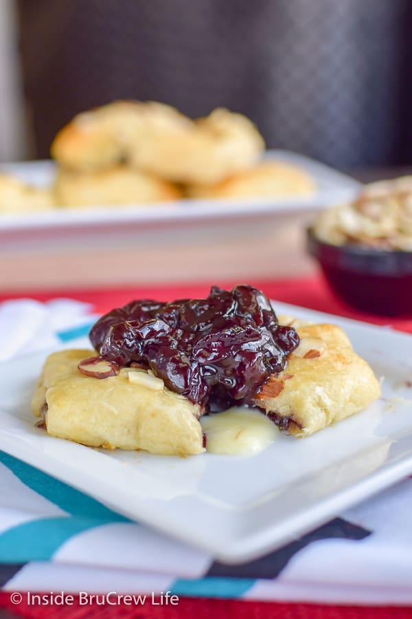 A white plate full of delicious cherry preserves on a cheesy croissant pocket.