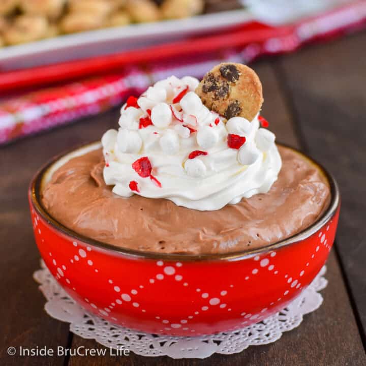 A red bowl filled with hot chocolate cheesecake dip and topped with whipped cream