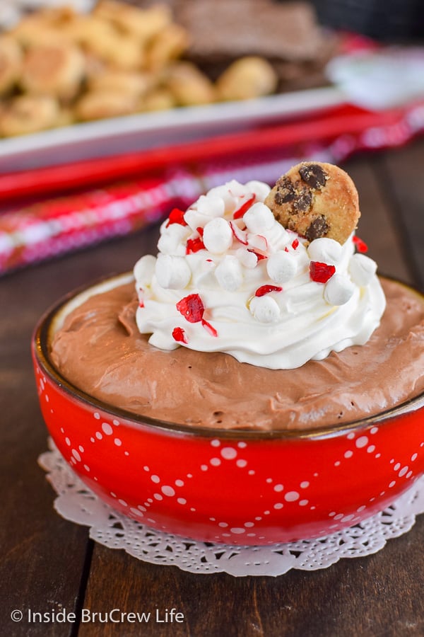 Close up picture of a red bowl filled with chocolate dip and topped with whipped cream and peppermint bits.