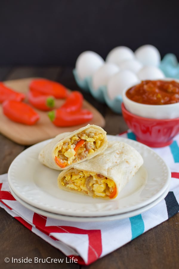 An egg burrito cut in half and stacked on a white plate with a bowl of salsa beside it.