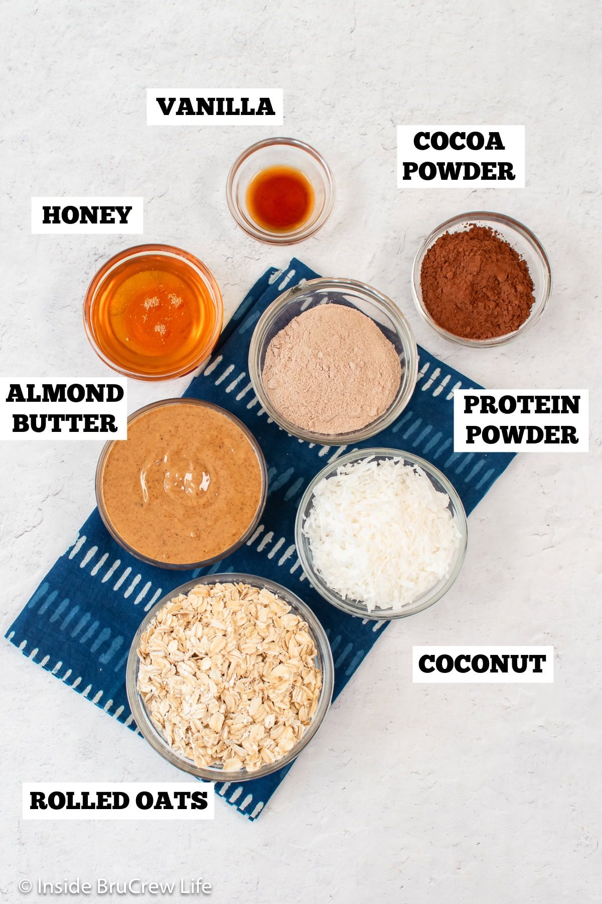A white board with bowls of ingredients needed to make almond joy energy bites.