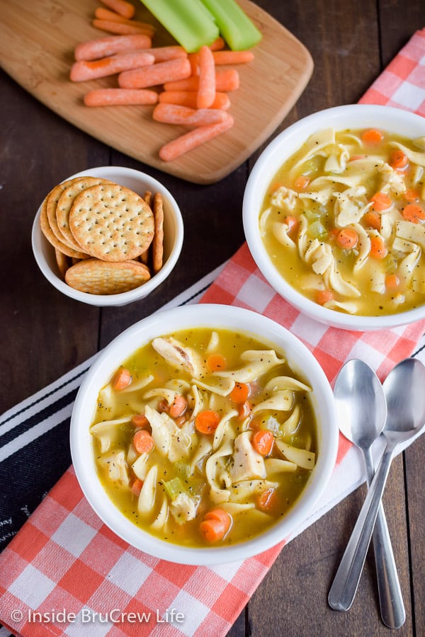 Two white bowls filled with chicken soup loaded with noodles and veggies.