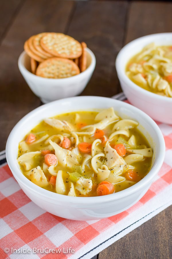 White bowls filled with homemade chicken soup on an orange and white towel.