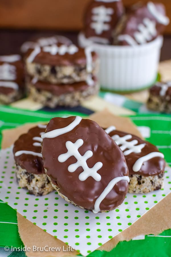 Football rice krispie treats stacked on a white and green paper.