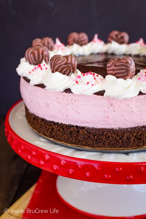 A white cake plate with red trim on it supporting a chocolate and strawberry dessert.