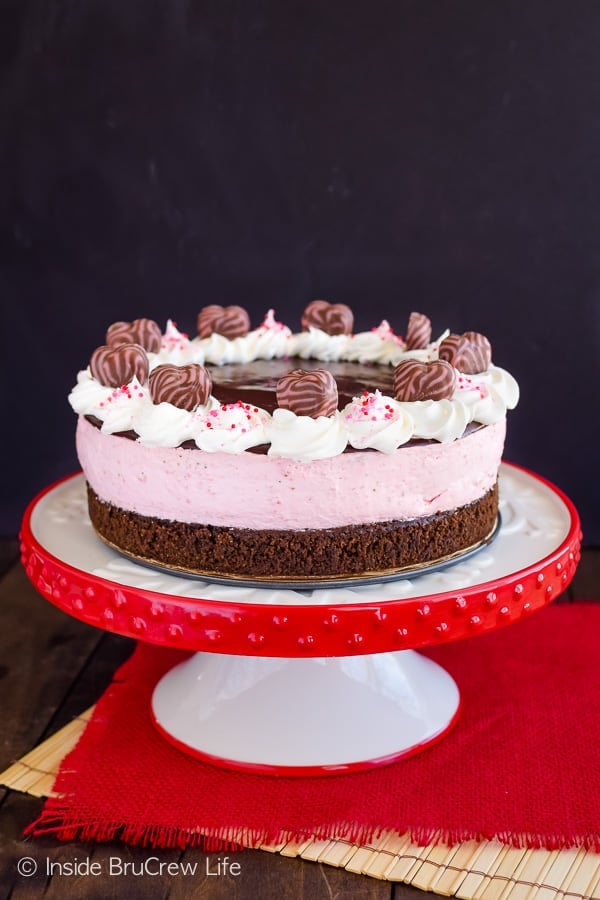 A white and red cake plate with an entire strawberry mousse brownie cake on it.