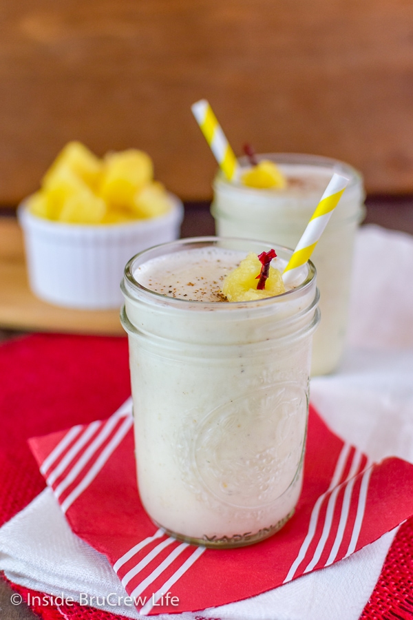 Two clear glasses filled with vanilla pineapple smoothie and topped with a straw and pineapple skewer