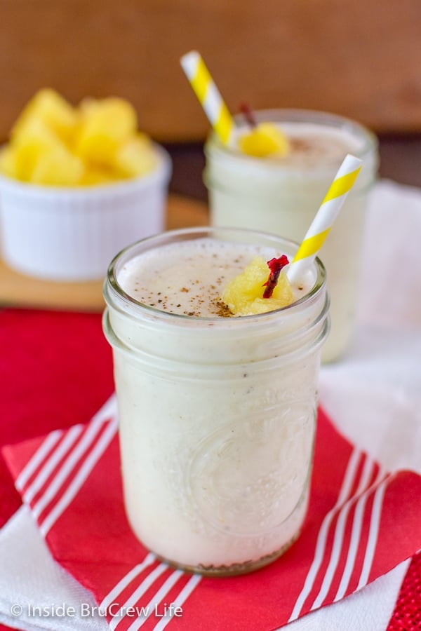 Two clear glassed filled with vanilla protein smoothie and topped with a straw and pineapple toothpick