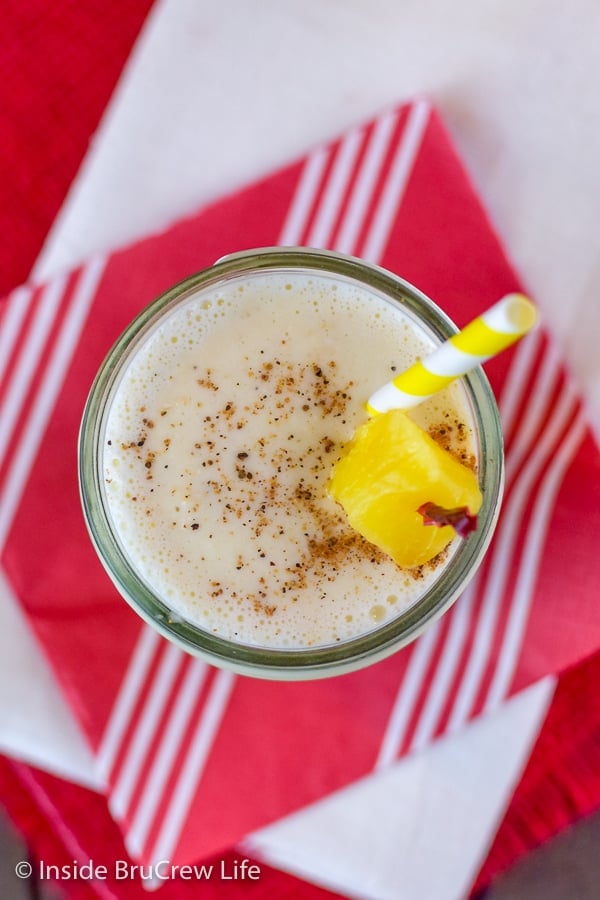 Overhead picture of a clear glass filled with vanilla pineapple smoothie on a red napkin