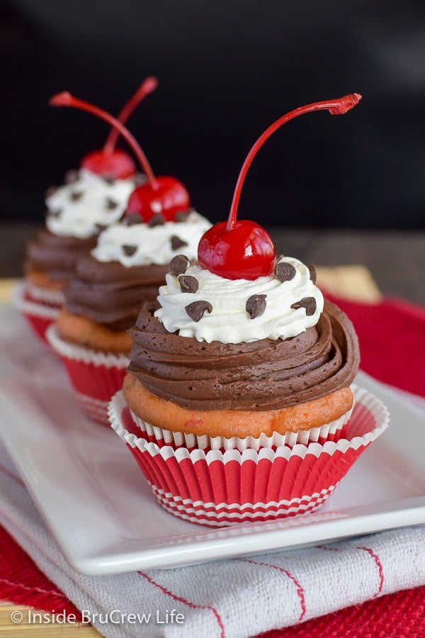 Cupcakes topped with chocolate and cherries in a red cupcake liner.