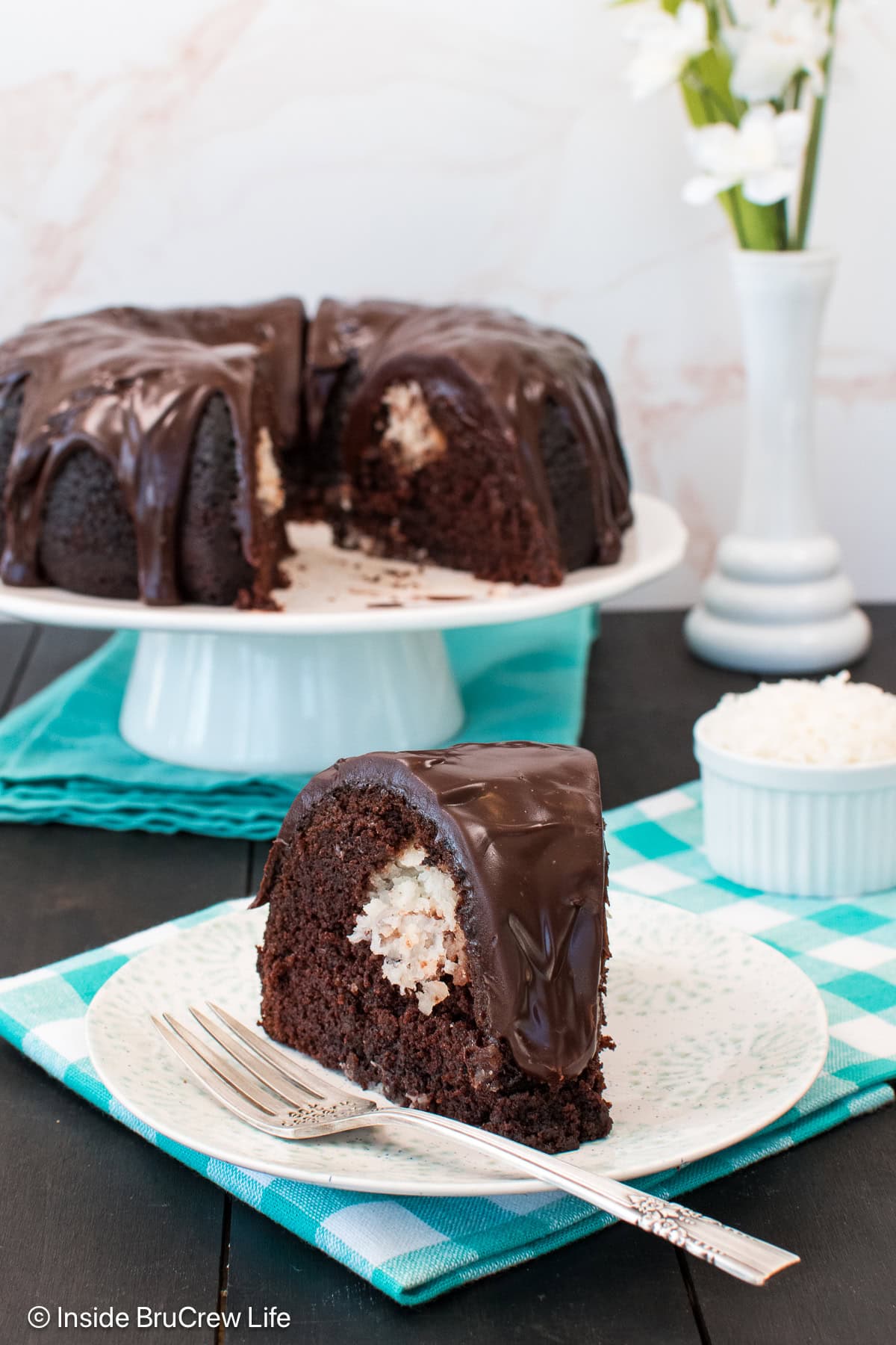 A chocolate bundt cake on a stand with a plated slice in front of it.