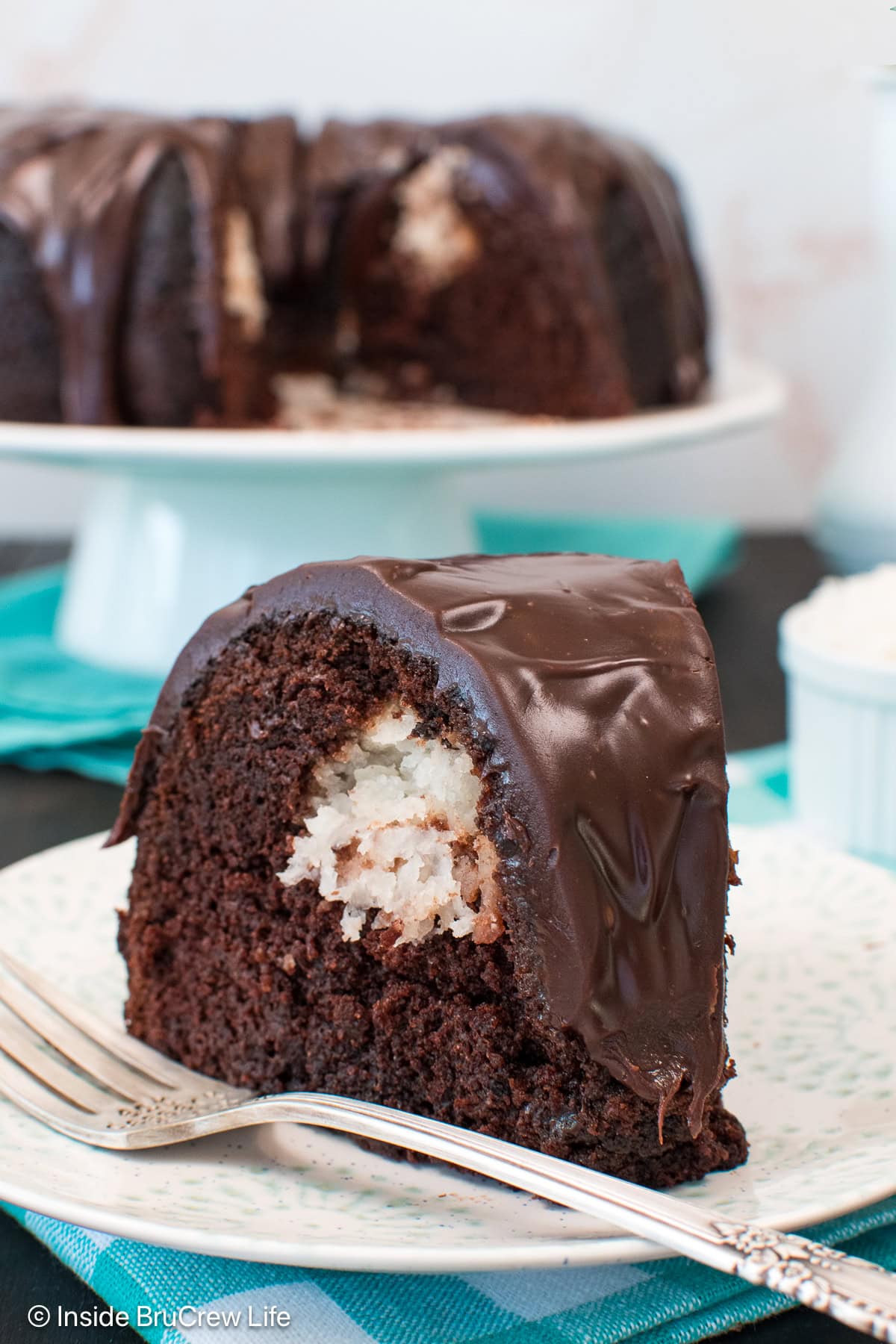 A white plate with a slice of chocolate coconut cake on it.