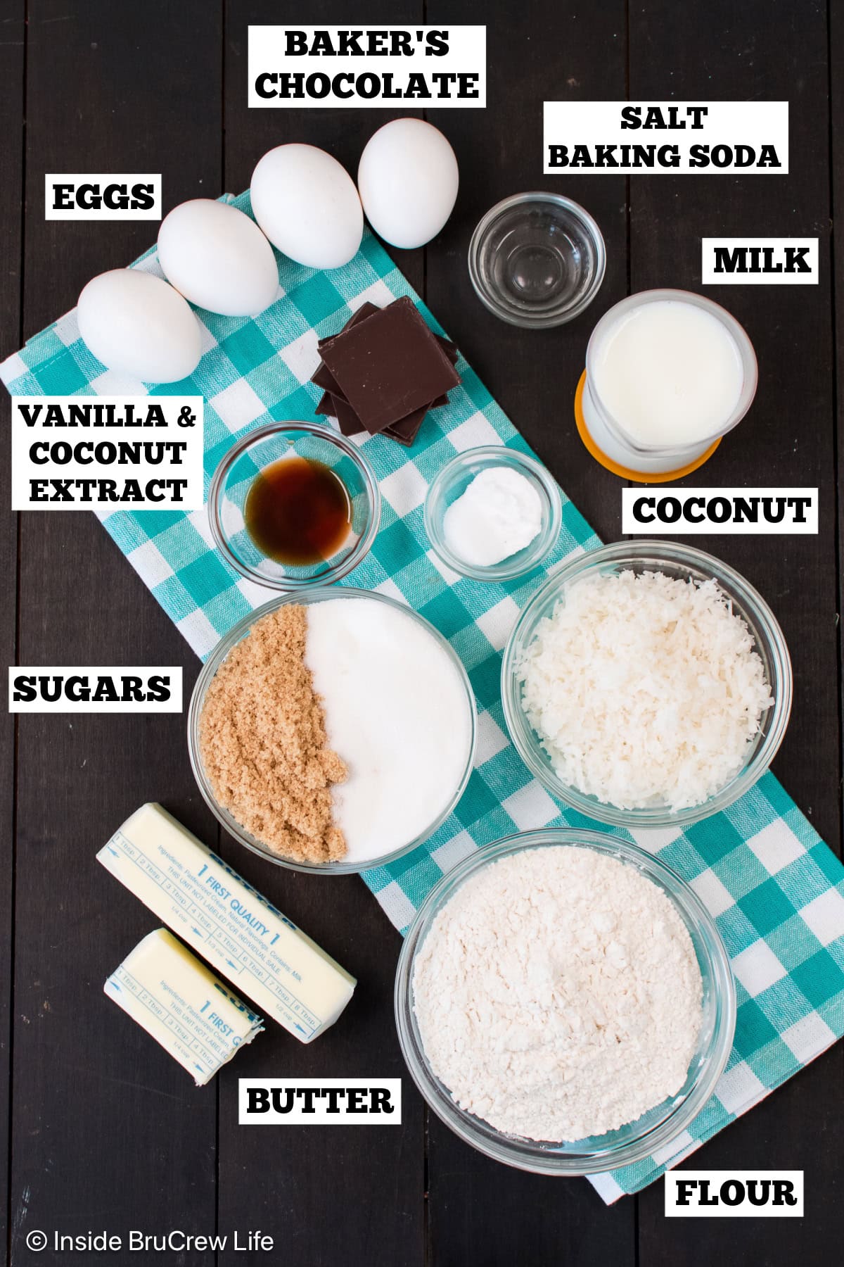 A brown board with bowls of ingredients needed to make a chocolate bundt cake with coconut.