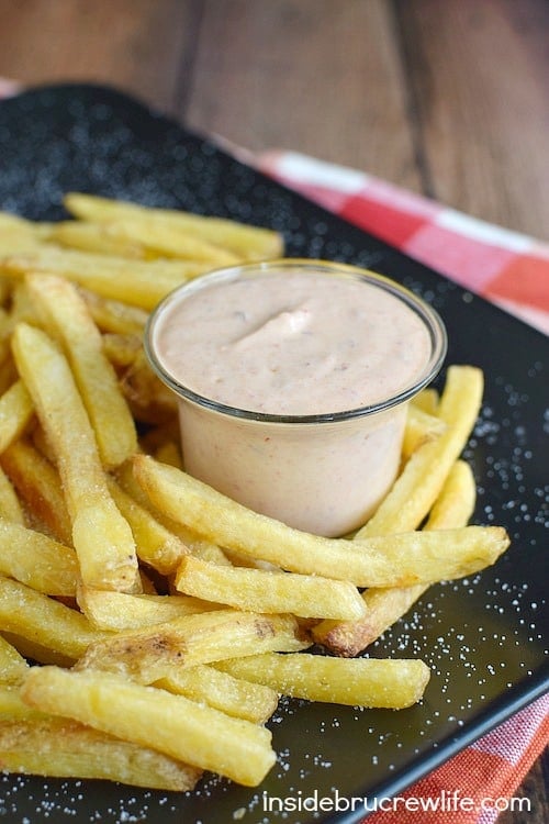 A black plate of fries with a dipping sauce.