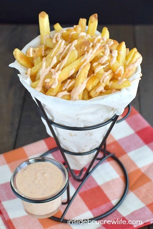A paper cone full of french fries and dipping sauce.