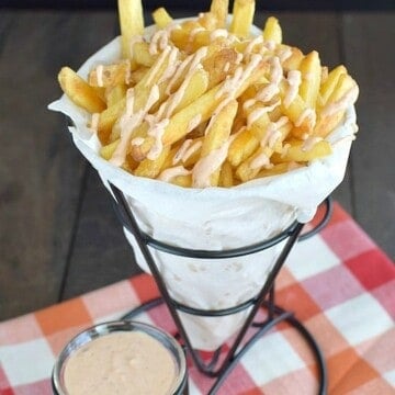 A paper cone full of fries and dipping sauce.