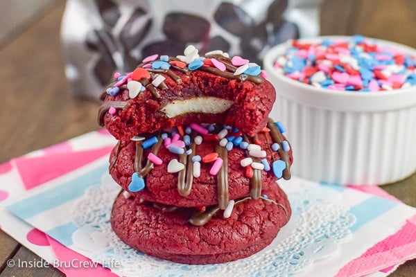 A white doily with three red velvet cookies stacked together and a bite out of the top showing the peppermint pattie inside
