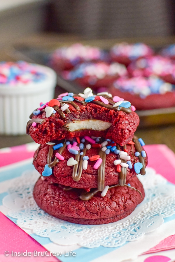 Blue and pink papers with three red velvet cookies stacked on them and a bite out of the top showing a peppermint pattie inside
