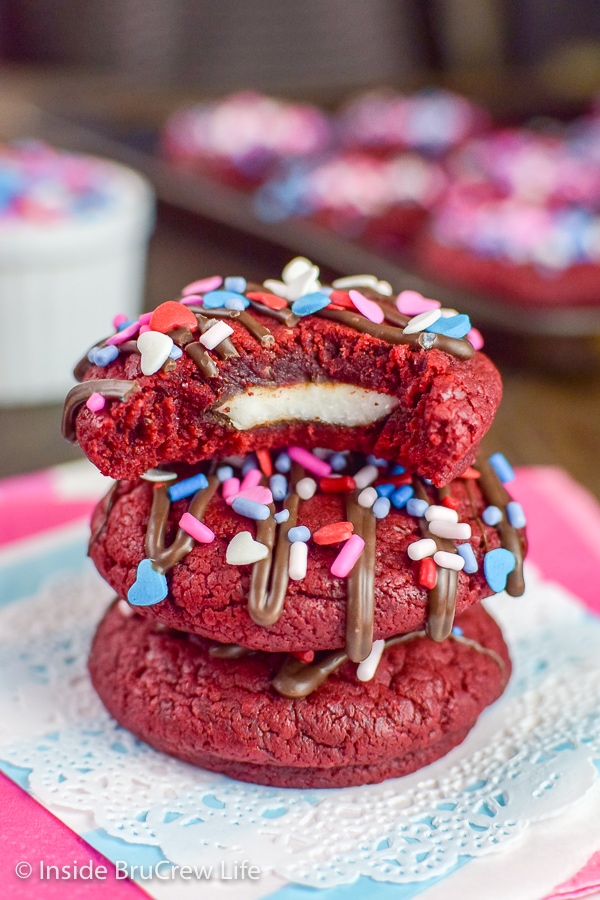 Three red velvet peppermint pattie cookies stacked on top of each other and a bite take out of the top showing the candy bar inside