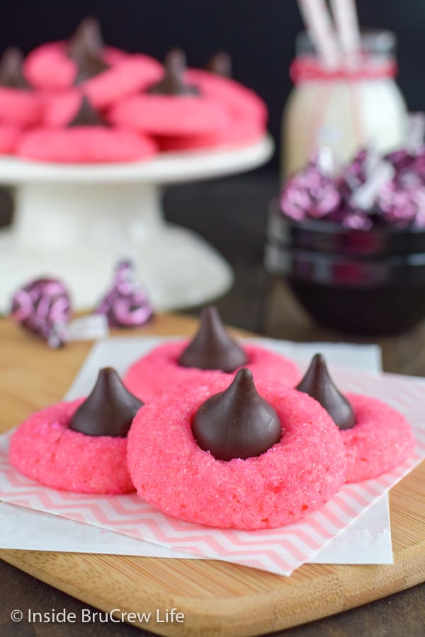 Pink cookies with chocolate kisses stacked on a wooden board.