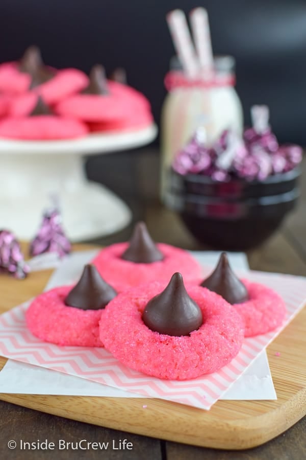 Pink cookies topped with a chocolate kiss stacked on a board.