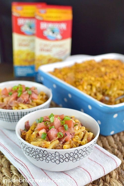 Two bowls of macaroni and cheese topped with bacon, onions, and tomatoes.