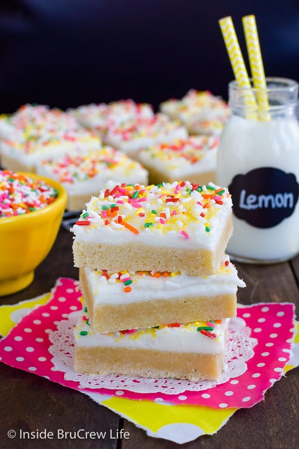 A stack of three lemon cookie bars topped with frosting and sprinkles.