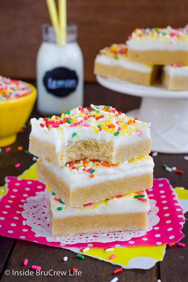 Three lemon cookie bars topped with frosting and stacked on top of each other.