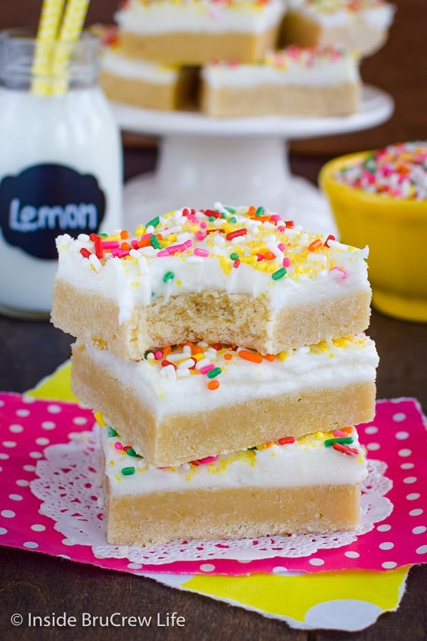 A stack of three frosted lemon cookie bars stacked on top of each other with a bite out of the top bar.