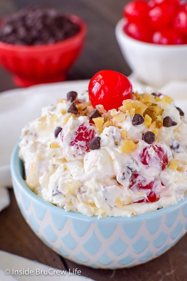 A close up picture of a blue and white bowl with a banana fluff salad topped with nuts, chocolate chips, and a cherry