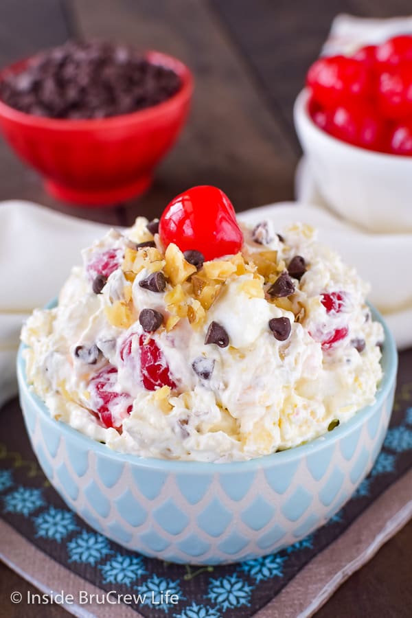 A blue and white bowl filled with banana fluff salad and topped with nuts, chocolate chips, and cherries