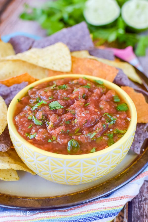 A yellow bowl filled with homemade salsa and chips around it