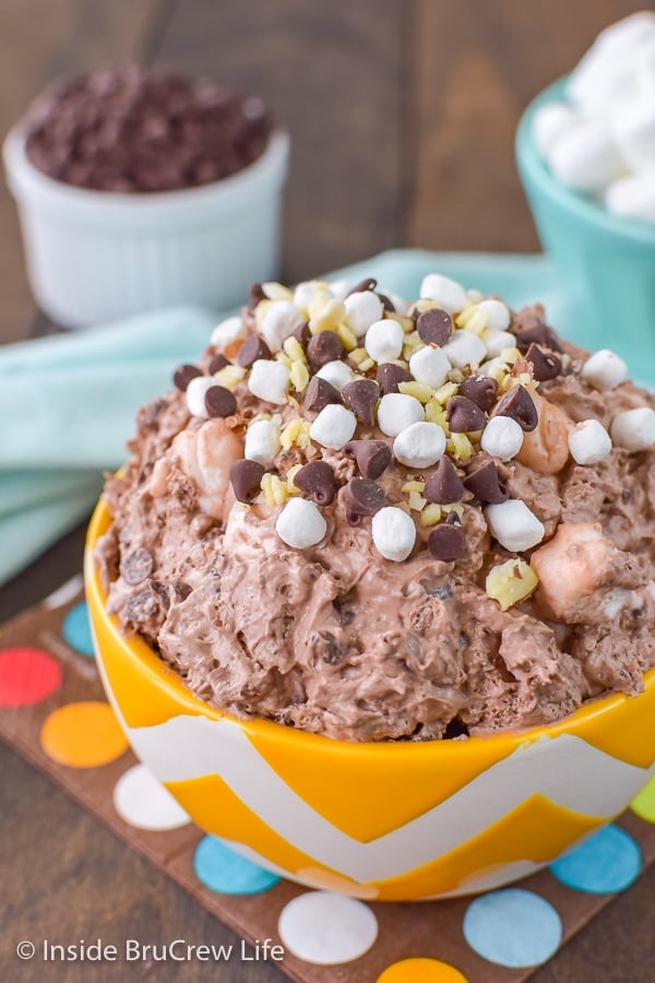 A yellow and white bowl filled with chocolate fluff and loaded with almonds, marshmallows, and chocolate chips.