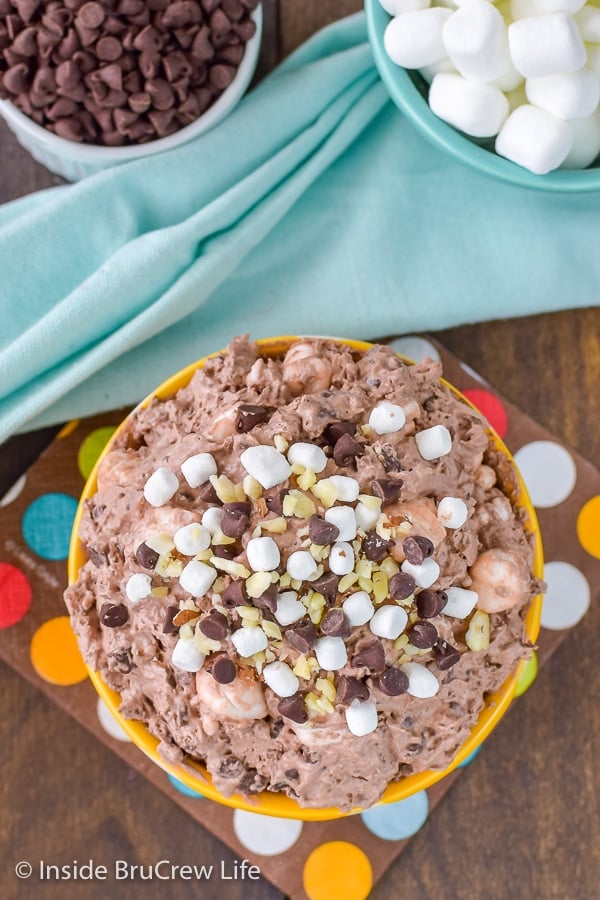 Overhead picture of a yellow bowl filled with chocolate fluff and topped with mini marshmallows, mini chocolate chips, and almond chunks