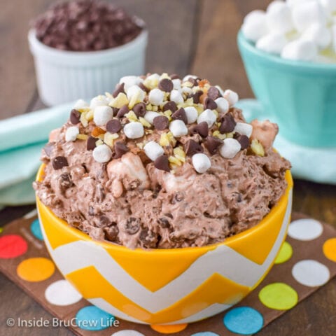 A yellow and white bowl filled with chocolate fluff loaded with almonds, chocolate chips, and marshmallows