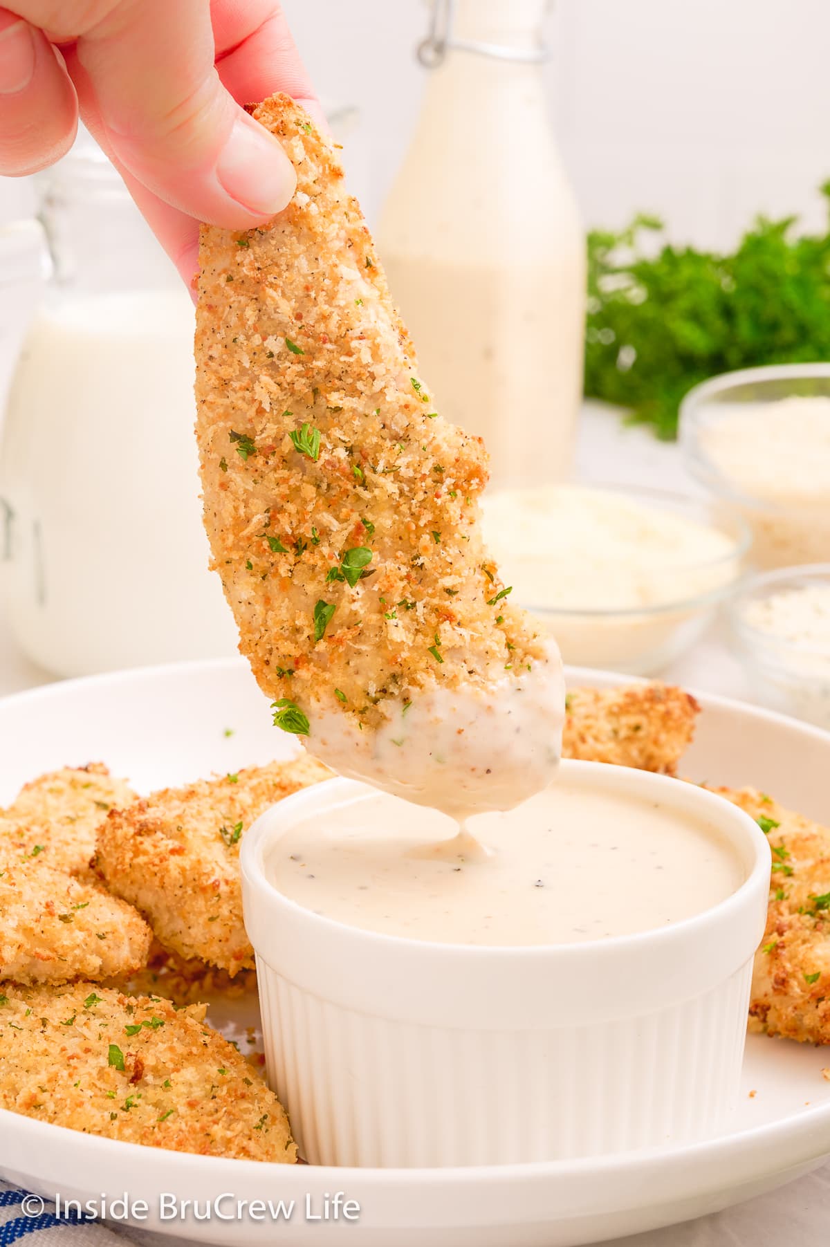A crispy chicken tender being dipped in ranch dressing.