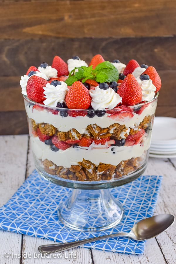 A blue towel with a clear dish on it filled with a berry trifle made from fresh fruit, no bake cheesecake, and oatmeal cream pies